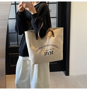 Close-up of cream canvas tote bag with brown leather straps and metal rivet detail