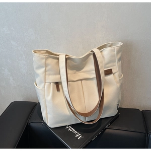 Detail view of canvas tote bag featuring side pockets and contrast brown straps