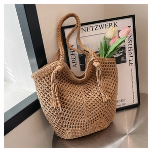 Detail of woven straw tote bag with hollow knit patterns and long decorative tassels