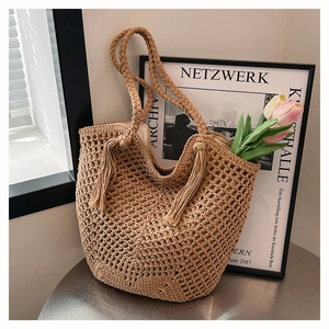Detail of hand-woven tote bag with braided handles and decorative tassel ornament