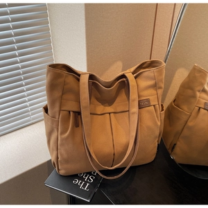 Detail of a brown canvas tote bag featuring pleated front design and side pocket