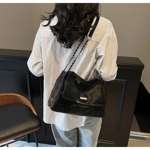 Rear view of a model wearing the large black glossy tote bag with metal chain strap