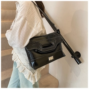 Detail of black glossy leather bucket bag with white contrast stitching and silver hardware