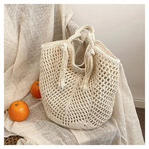 Detail of hand-woven cream tote bag with hollow mesh texture and long side tassels