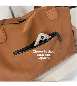 Close-up of front zipper pocket on brown leather tote bag with a phone for scale