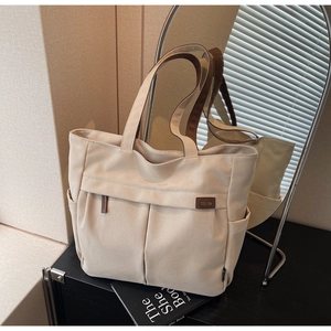 Detail of off-white canvas tote bag featuring brown brand label and exterior pockets
