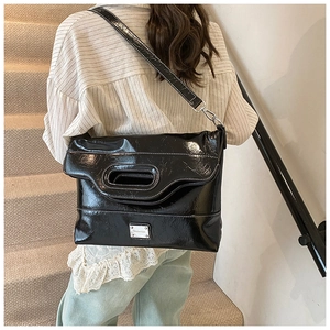 Detail of black patent leather bucket bag featuring white stitching and silver logo plate