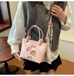Gros plan sur un sac seau rose avec broderie florale et détails dorés