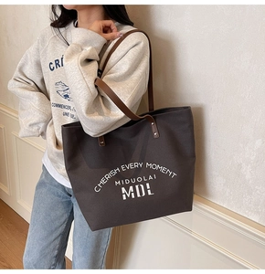 Detail view of large brown canvas tote bag with leather straps and printed text