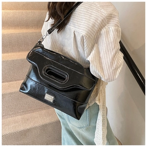 Detail view of black patent leather tote with white contrast stitching and oval handle cutout