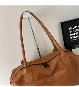 Detail of caramel brown tote bag featuring dual zippers and reinforced handle stitching