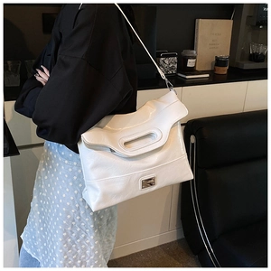 Detail view of large white patent leather bucket bag with metallic twist lock and hollow handle