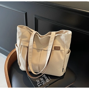 Detail of beige canvas tote bag with brown leather trim and pleated front on a chair