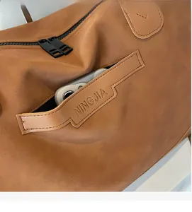 Close-up of brown textured leather side pocket with metal zippers and embossed strap detail