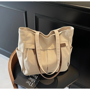Close-up of beige canvas tote bag featuring brown leather handles and side pocket detail