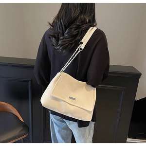 Detail of a large off-white leather tote bag with silver chain strap worn by a model