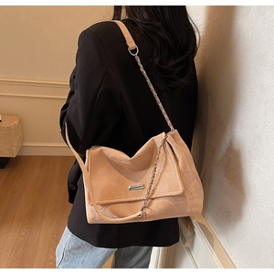 Close-up of apricot suede tote bag with metal chain detail and silver logo plaque