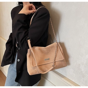 Detail of the suede tote bag showing chain strap and metallic brand plate on beige leather