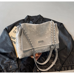Close-up of a silver-grey velvet tote bag with a chain strap on a black leather jacket