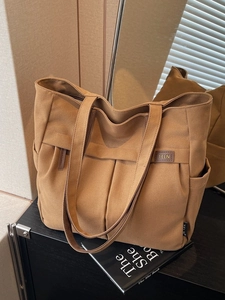 Large khaki canvas tote bag with front pleats and leather TELN logo on a black surface