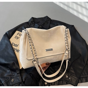 Detail of off-white faux leather tote with metal logo and chain strap on black background
