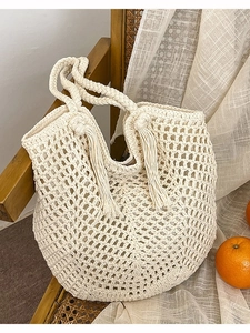 Handmade crochet tote bag in beige with fringe tassels hanging on a vintage wooden chair