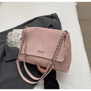 Detailed view of dusty pink suede shoulder bag with gold chain and metal emblem