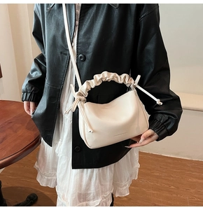 Close-up of cream ruched handle pillow bag with fashion lettering and bow details