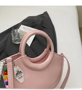 Detail of light pink half-moon handbag with smooth leather texture and beaded charm