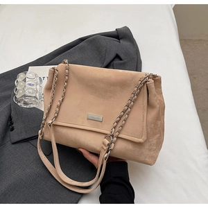 Close-up of beige suede chain tote bag featuring a silver engraved metal logo plaque