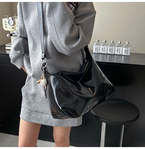 Close-up of black glossy tote bag featuring a decorative baseball charm and shoulder strap