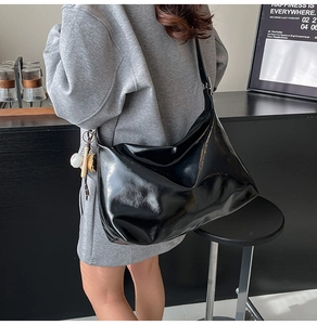 Detail of glossy black hobo shoulder bag with baseball charms on model side view