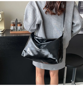 Close-up of a large black glossy crossbody tote bag worn over a grey sweatshirt