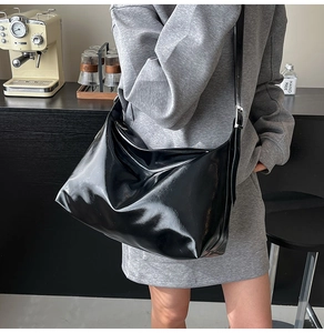 Close-up of a large black glossy patent leather tote bag on a crossbody shoulder strap
