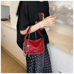 Detail of red patent leather handbag with silver chain strap and metal fashion plaque
