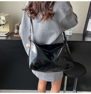 Chic black patent leather hobo bag with baseball charm shown on shoulder in a cafe