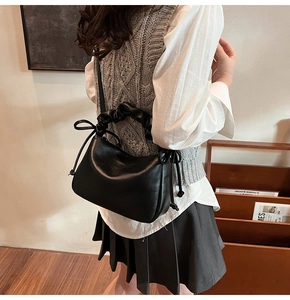 Detail of black pleated handle handbag with drawstring bow and smooth faux leather texture
