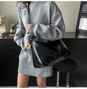 Detail shot of a black high-gloss tote bag with a decorative charm in a modern cafe setting