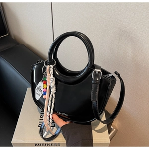 Close-up of black patent leather crescent bag with round handle and decorative charms