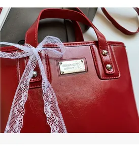 Detailed close-up of glossy red leather bucket bag with silver metal logo plate and lace bow