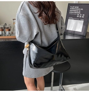 Glossy black patent leather tote bag styled with a grey hoodie in an urban setting