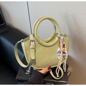 Detail of avocado green bucket bag featuring a circular handle and colorful beaded charm