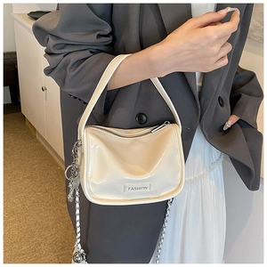 Detail of a creamy glossy leather handbag with a metal chain and a FASHION label