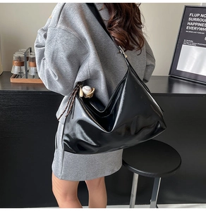 Detail of black glossy leather tote bag featuring a baseball charm and braided strap