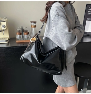 Close-up of black glossy patent leather tote bag with stylish pleated texture details