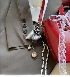 Close-up of silver bow and heart pendant charm hanging on a luxury red leather bag