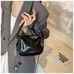 Detail of black patent leather handbag with silver chain and Fashion logo tag