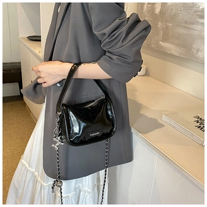 Detail of black patent leather crossbody bag with chain strap and bear charm