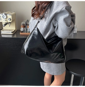 Side view of large black patent leather tote bag with glossy finish and minimalist design