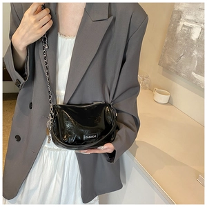 Detail of glossy black patent leather handbag with silver chain and Fashion label